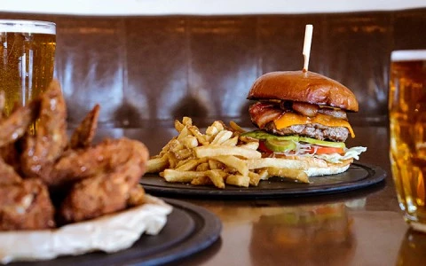 A burger, fries, chicken wings, and beer on a table in a booth.
