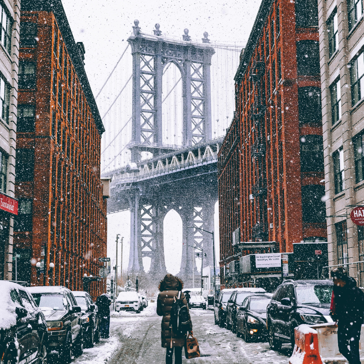 a woman on a bicycle in a snowy city with Manhattan Bridge in the background