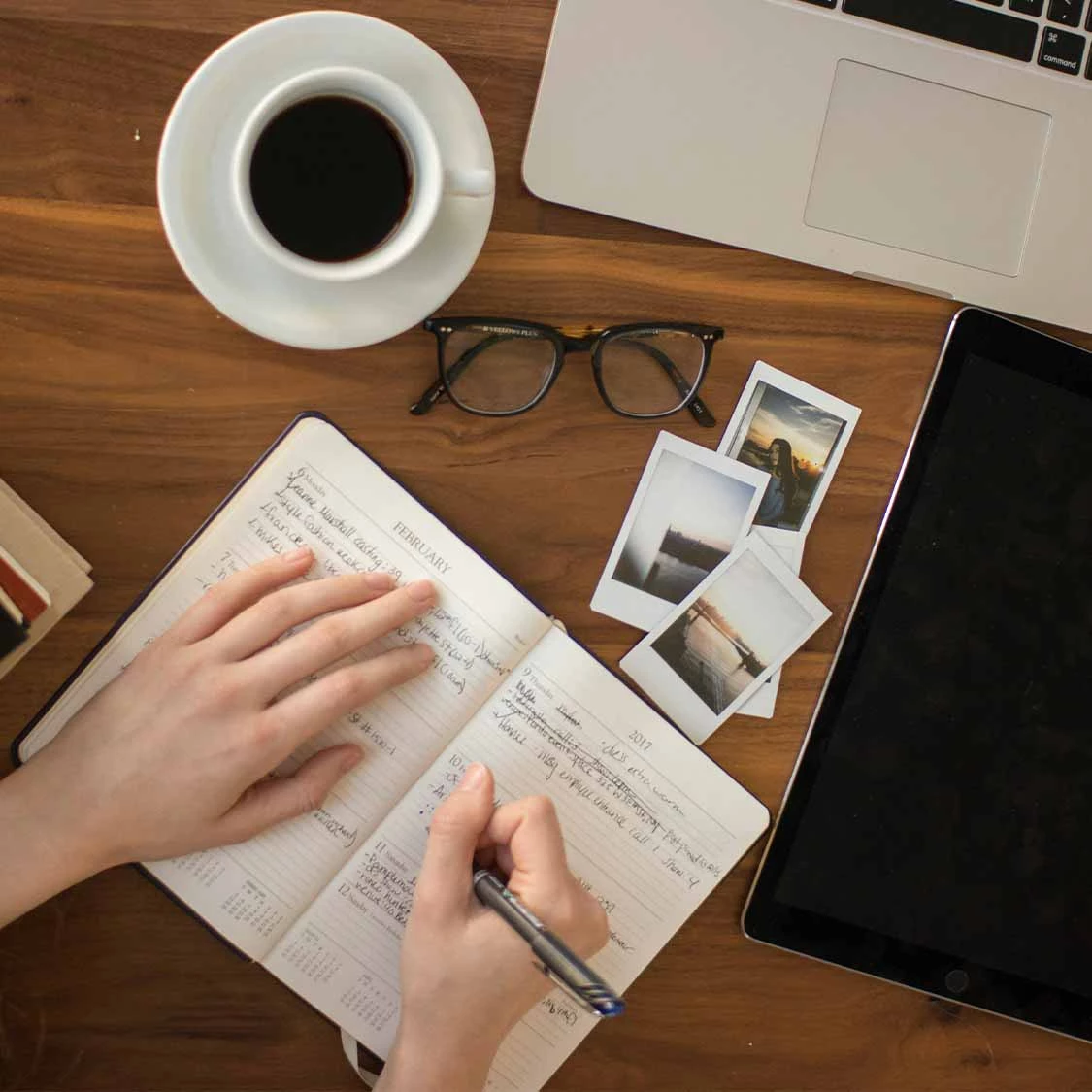 a hand writing in a notebook next to a laptop and a cup of coffee