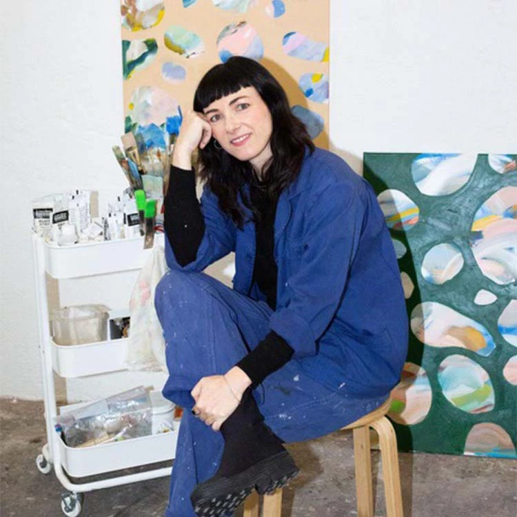 a woman sitting on a stool in front of a painting