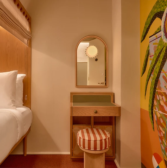 A hotel room with a bed, desk, mirror, and stool