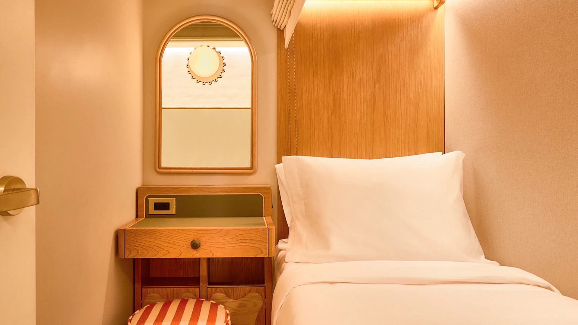 A compact hotel room with a single bed, a small wooden nightstand, and a mirror on the wall.