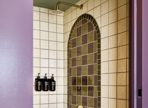 A shower with tiled walls and bottles on the wall