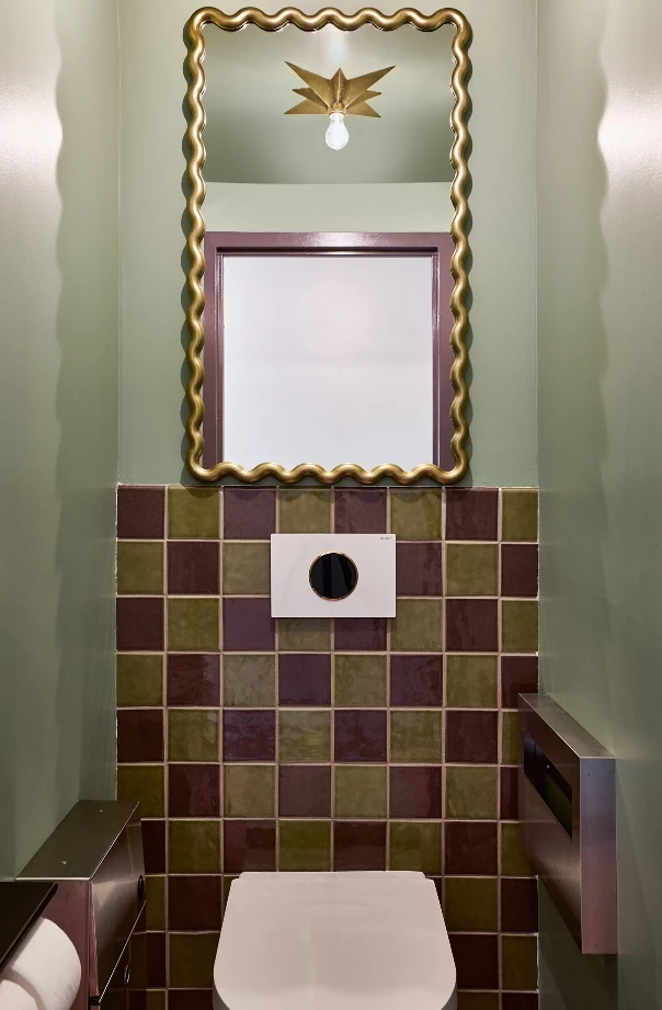 A bathroom with a toilet, tiled wall, and gold-framed mirror
