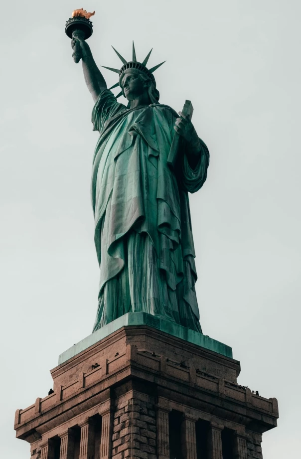 The Statue of Liberty stands tall with her torch and crown, set against a gray sky.