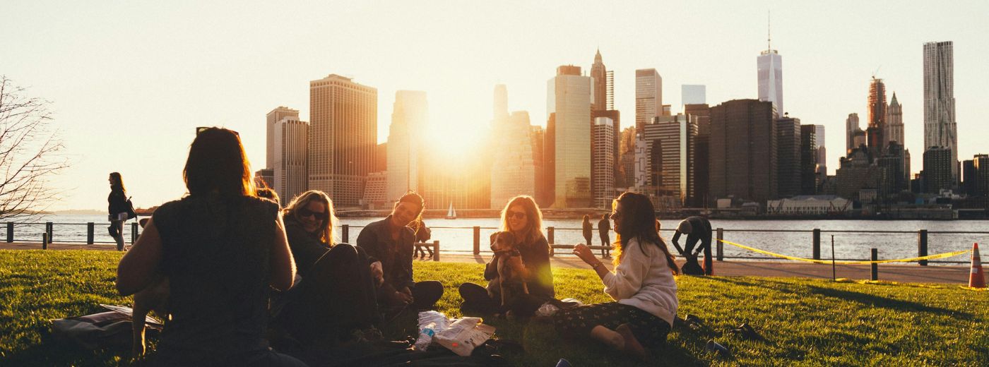 a group of people sitting on grass with a dog in front of a city