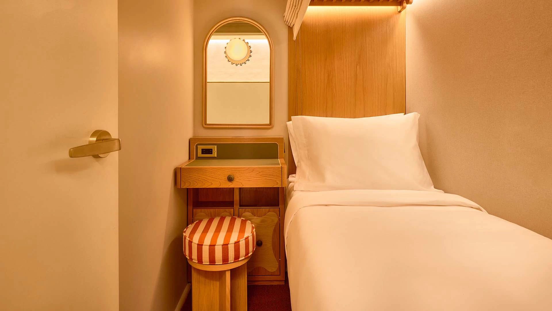 A small hotel room with a single bed, wooden headboard, and a mirror above a desk.