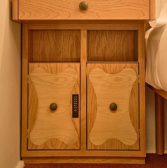 A wooden cabinet with a safe and brass knobs next to a bed.