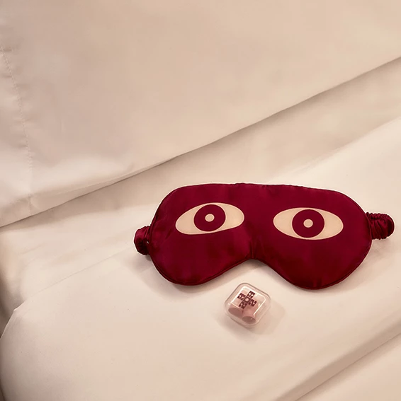A red eye mask and a small dice on a white bed.