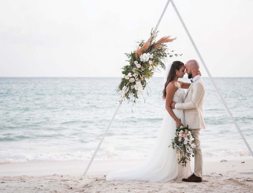 bride and groom posing under triangle on the beach