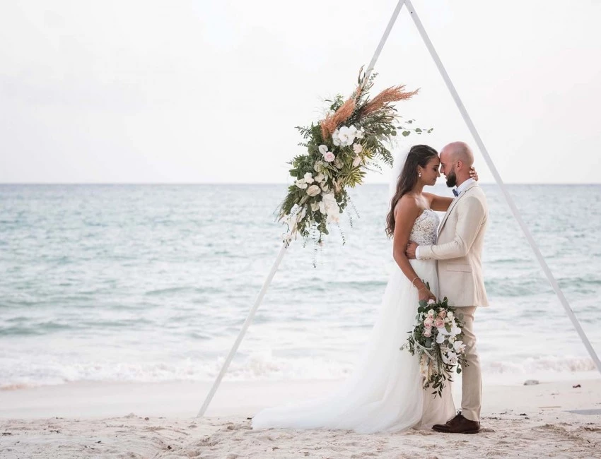bride and groom posing under triangle on the beach