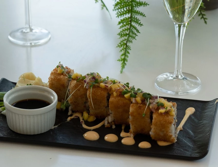 a plate of sushi with sauce and a glass of wine