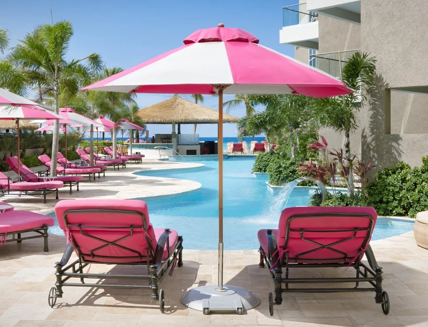 a pink lounge chairs and umbrella by a pool