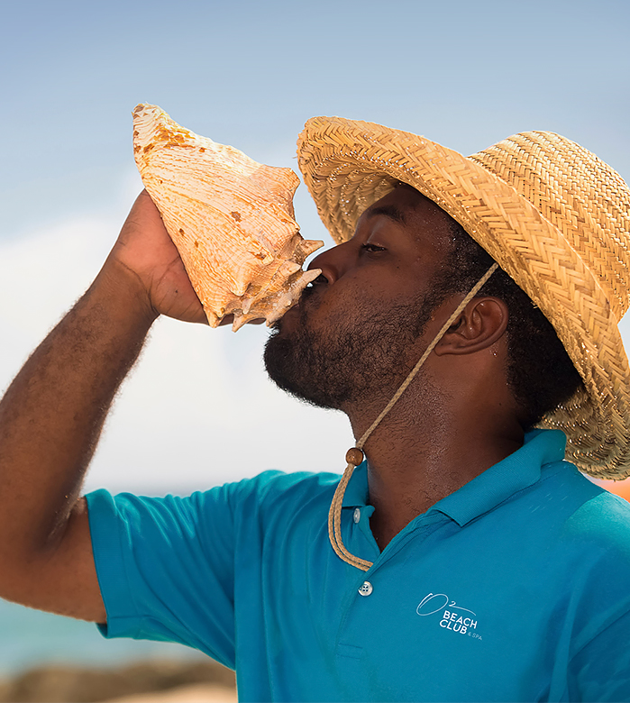 resort employee blowing into an orange conch shell