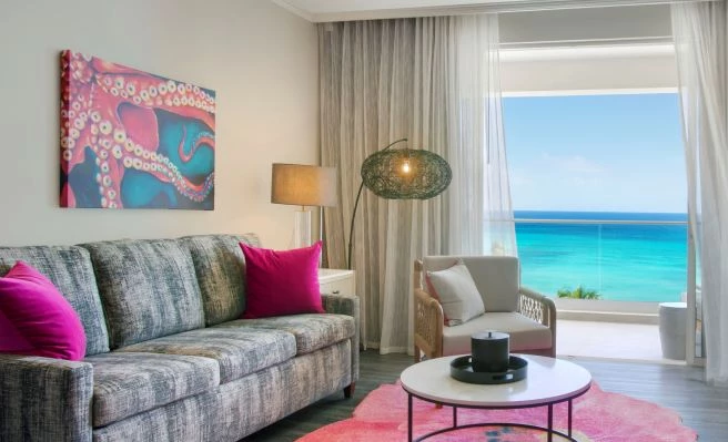 guest room with grey couch and hot pink pillows with a view overlooking the ocean