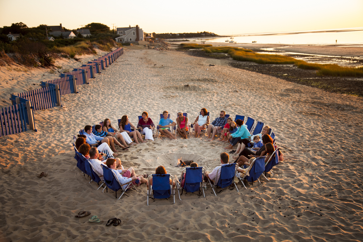a group of people sitting in chairs around a fire pit on a beach