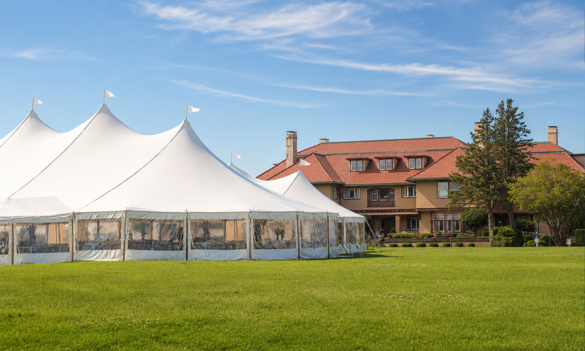 a large white tent in a grassy area with a house in the background