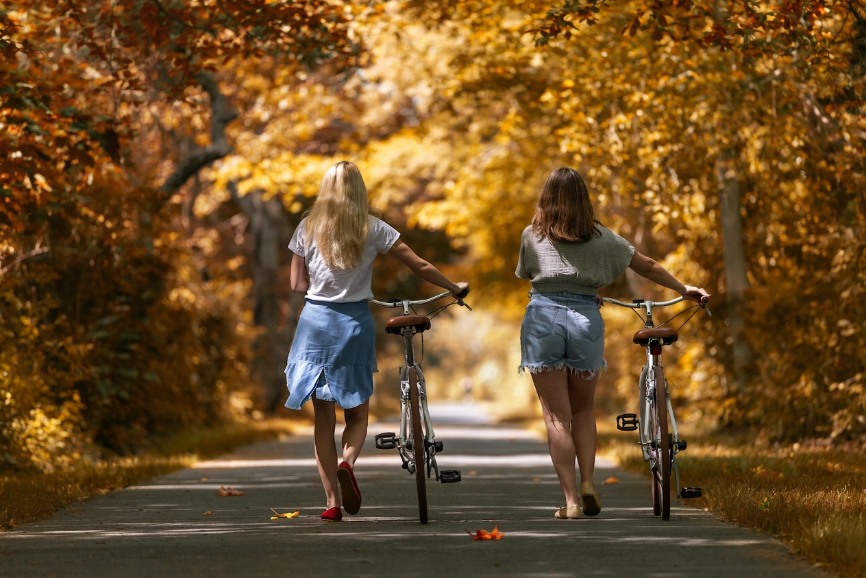 two women walking with bicycles on a path