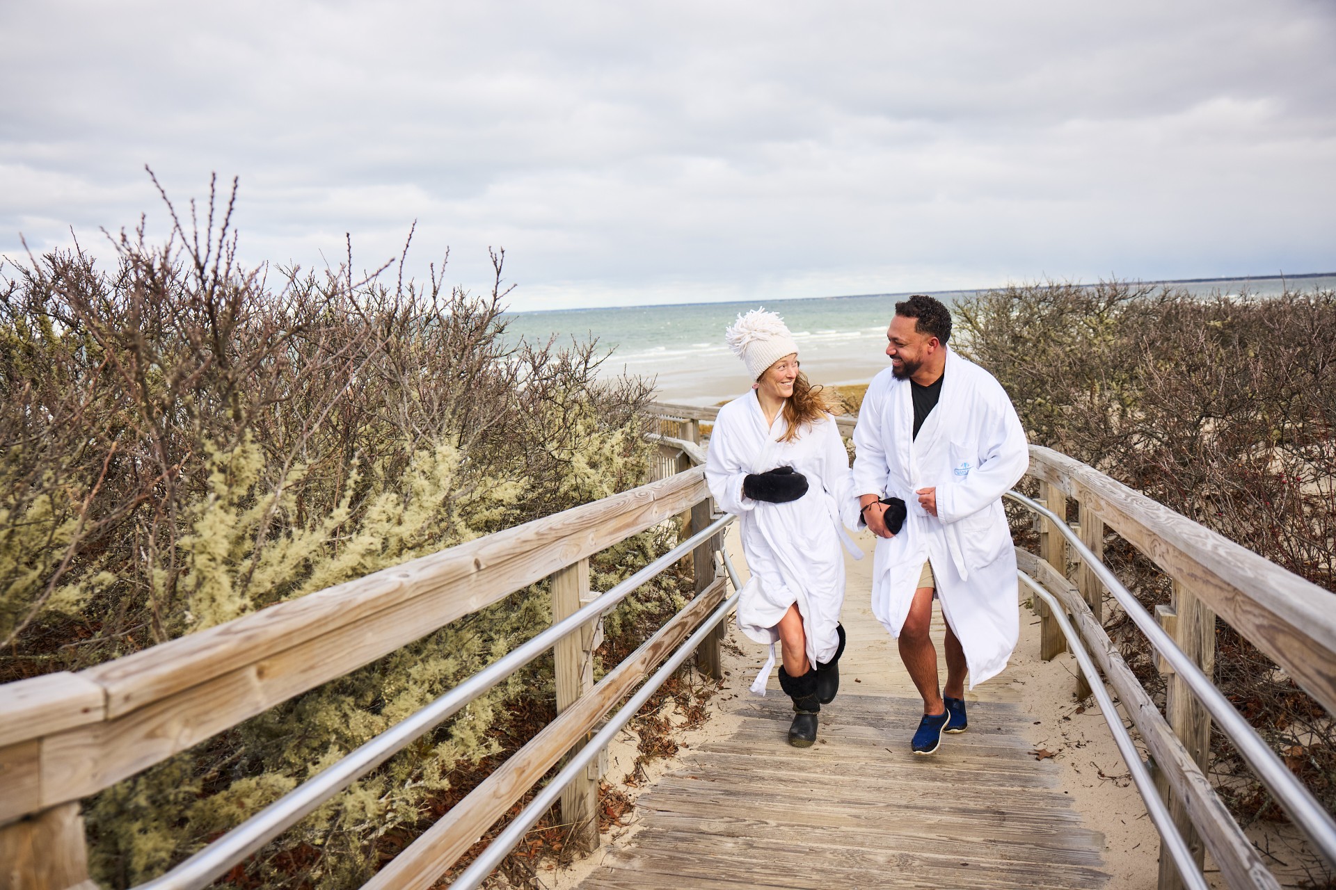 a man and woman wearing white robes walking on a wooden walkway