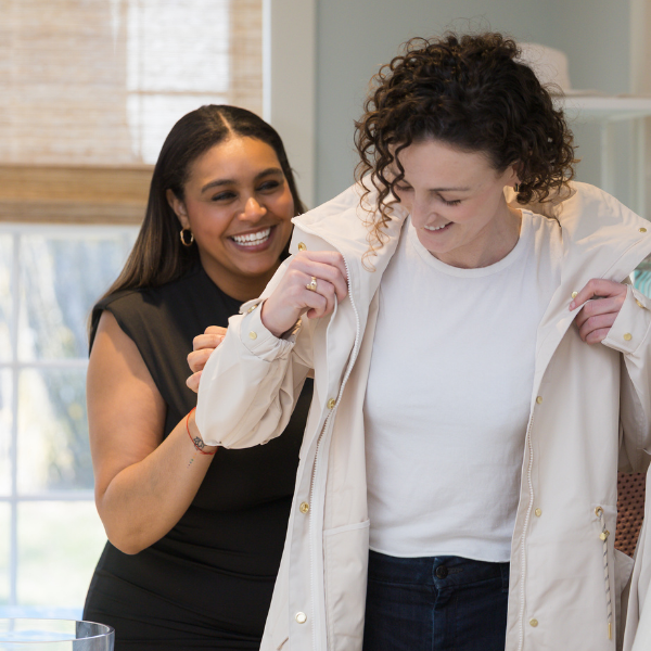 a woman helping another woman buttoning up a jacket