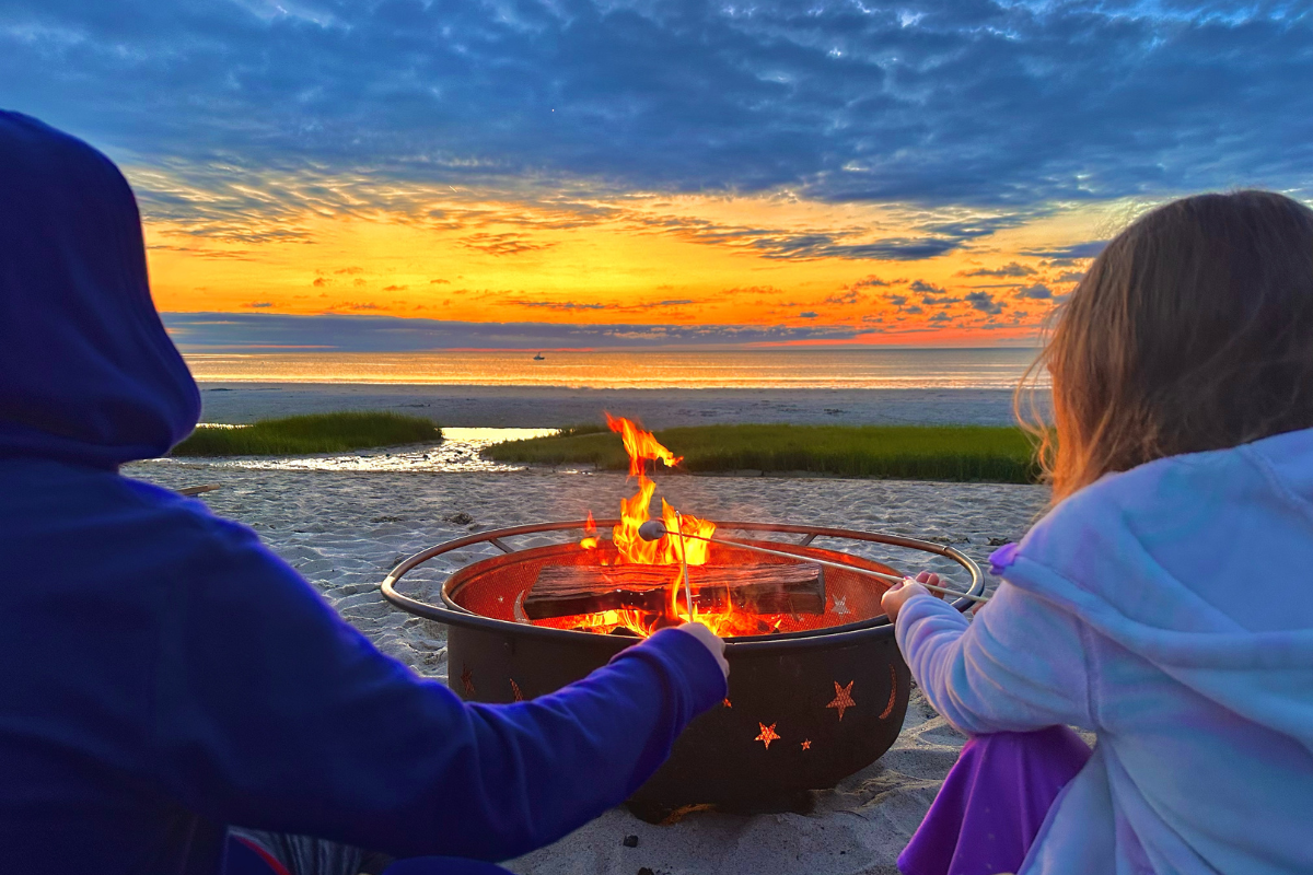 a couple of people sitting around a fire pit on a beach