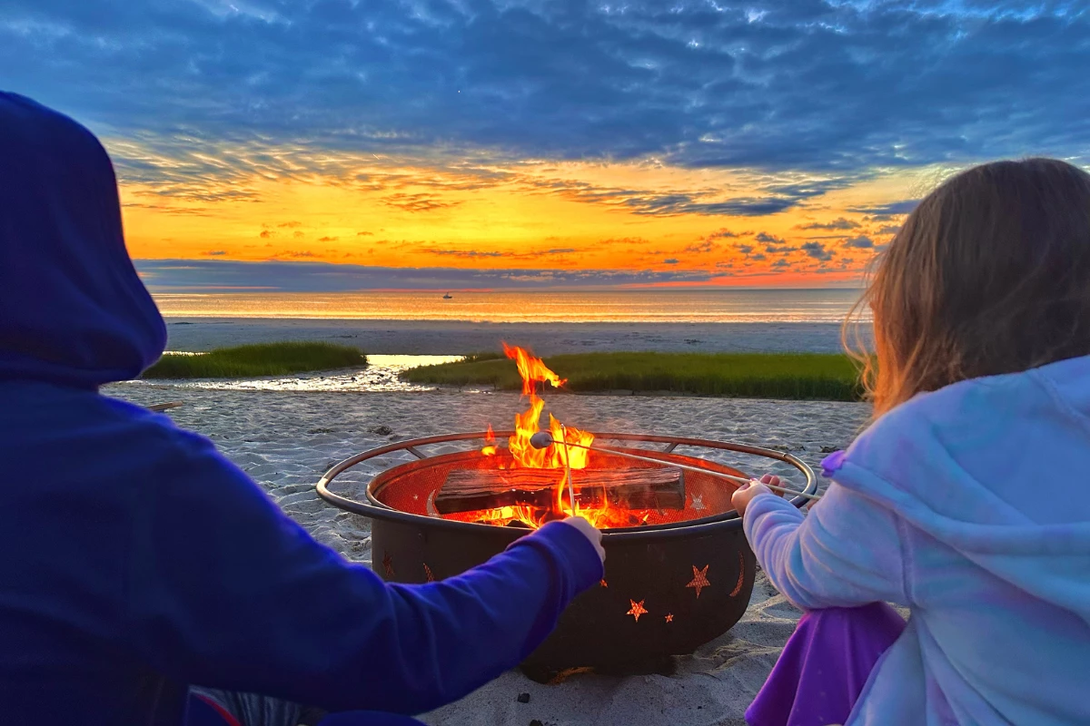 a couple of people sitting around a fire pit on a beach