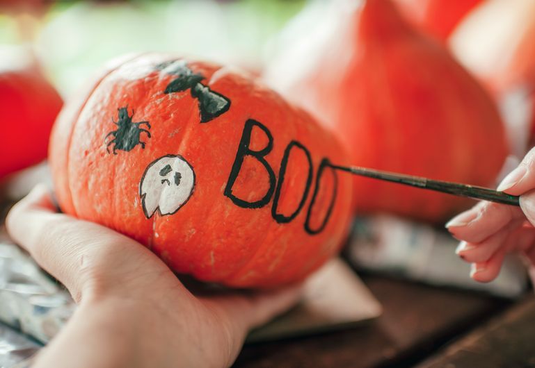 Painting a mini pumpkin with the word boo written on it 