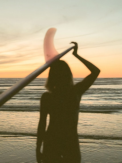 a silhouette of a woman holding a surfboard over her head