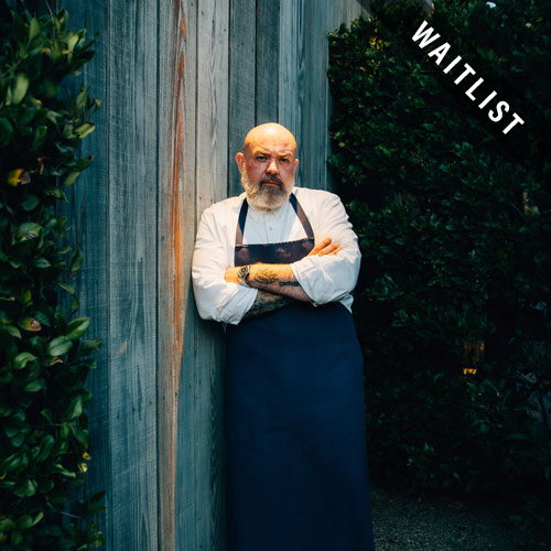 a man wearing an apron leaning against a fence