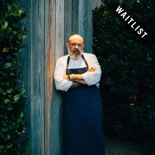 a man wearing an apron leaning against a fence