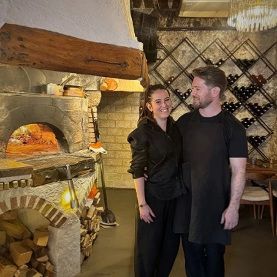 a man and woman standing in a room with a brick oven