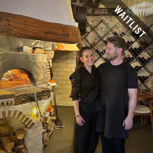 a man and woman standing in a room with a brick oven