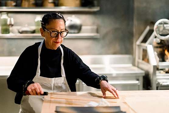 Elderly woman wearing black glasses cutting something with a big knife in the kitchen