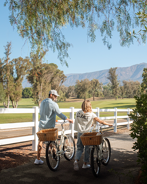 a man and woman with bicycles and a white fence