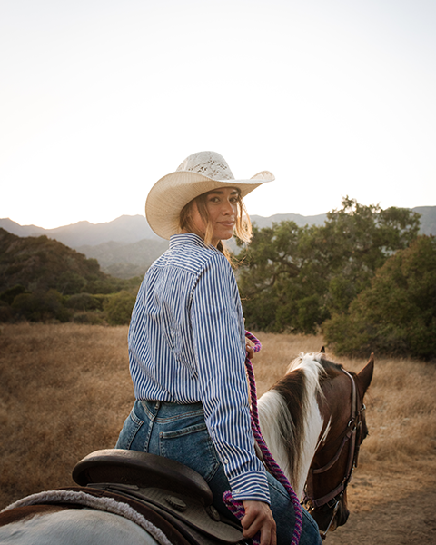 a woman wearing a cowboy hat and sitting on a horse