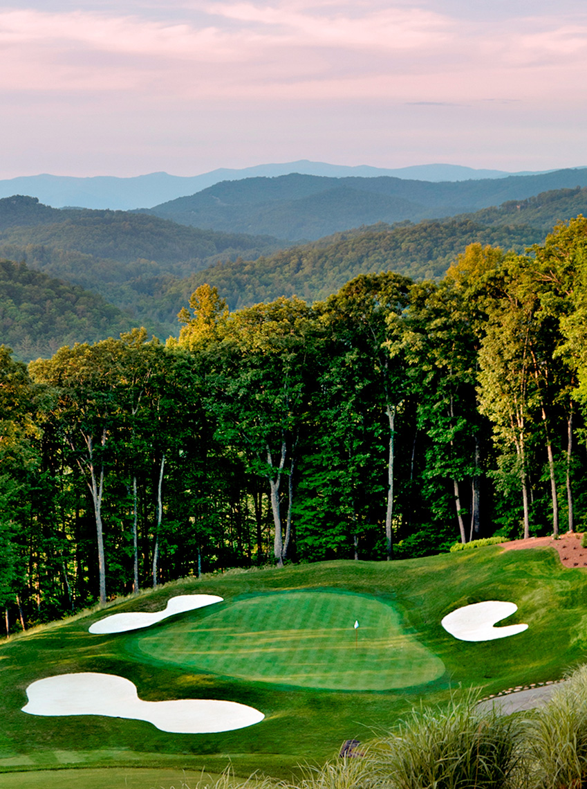 a golf course with trees and mountains in the background