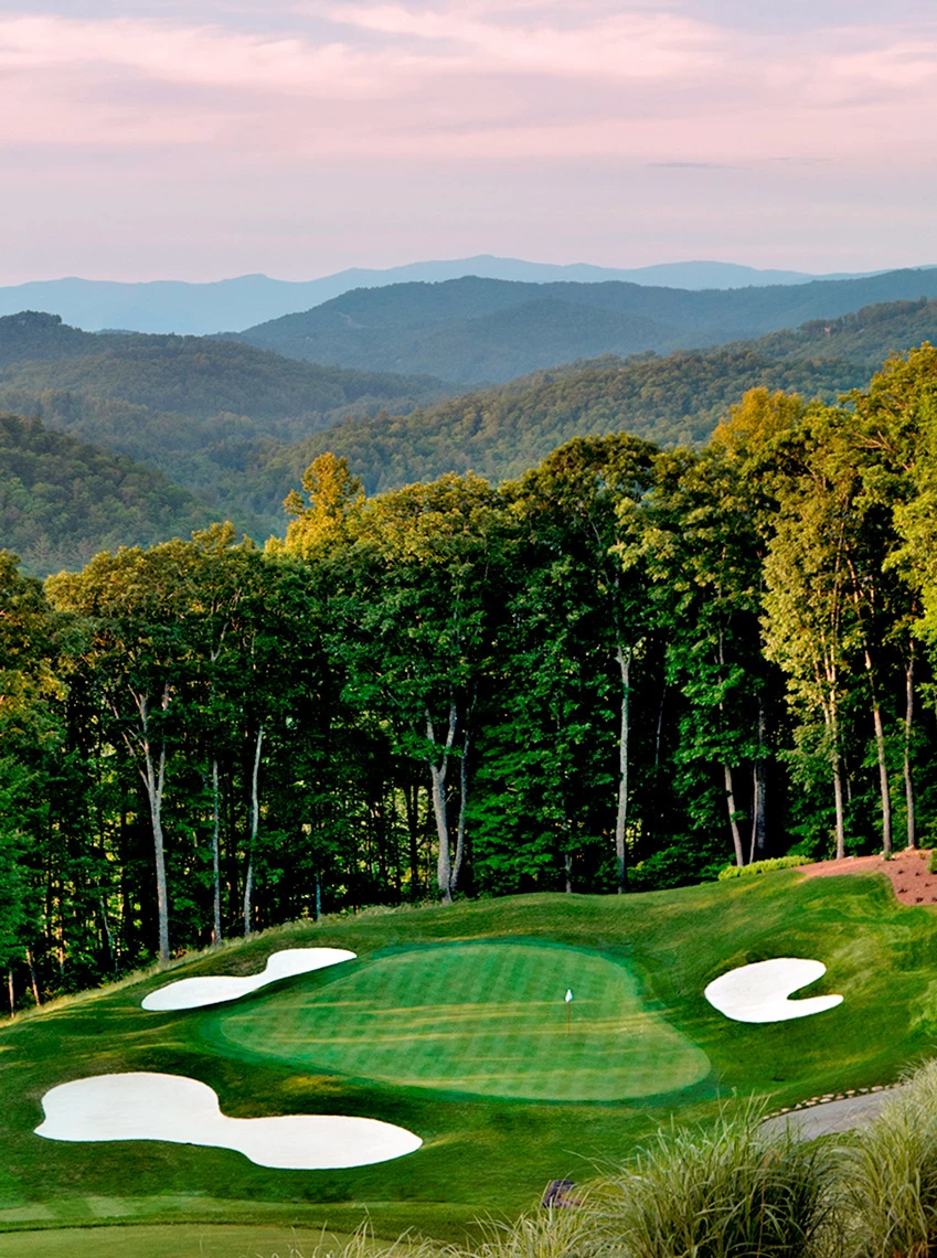 a golf course with trees and mountains in the background