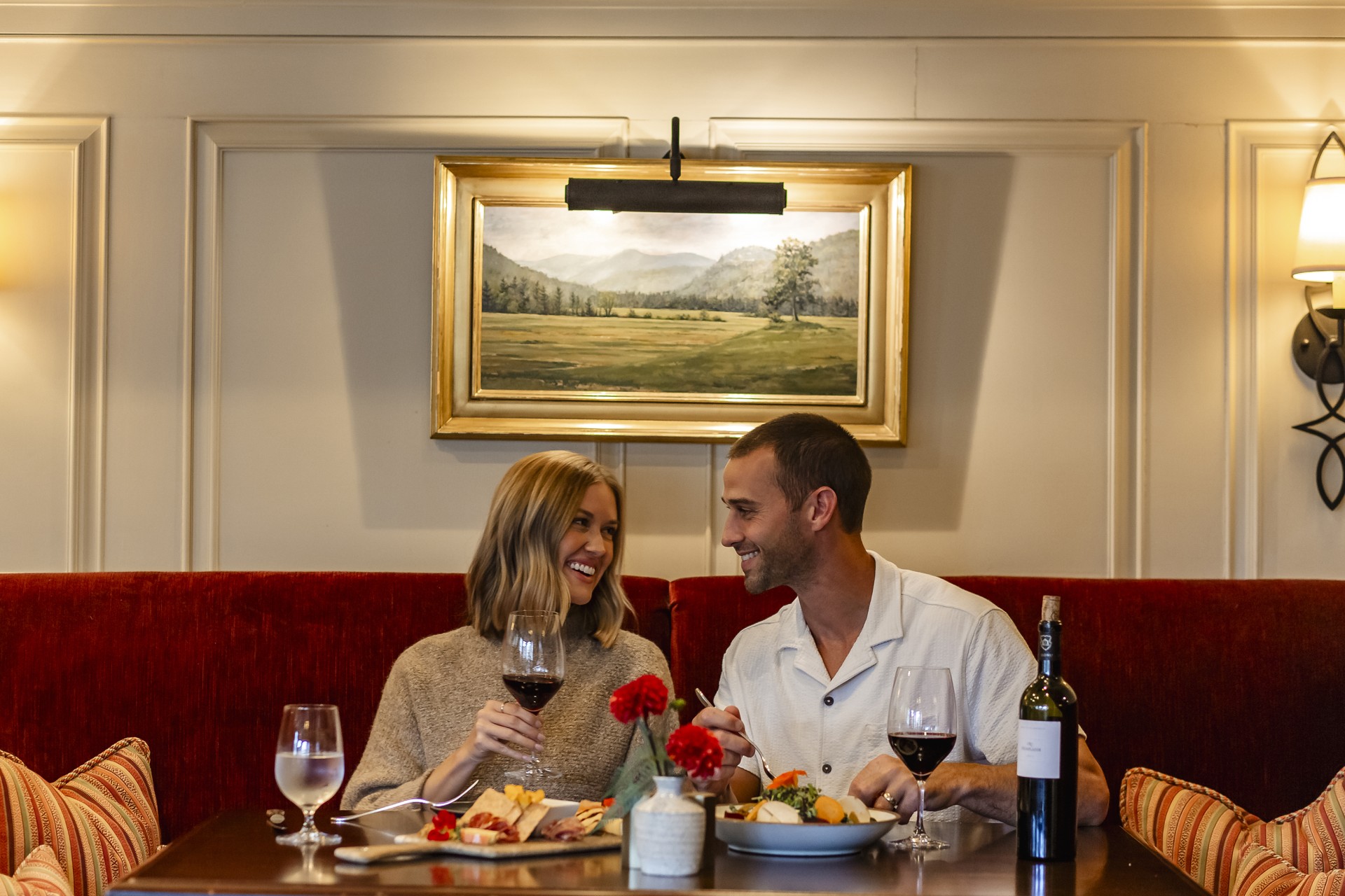 a man and woman sitting at a table with food and wine