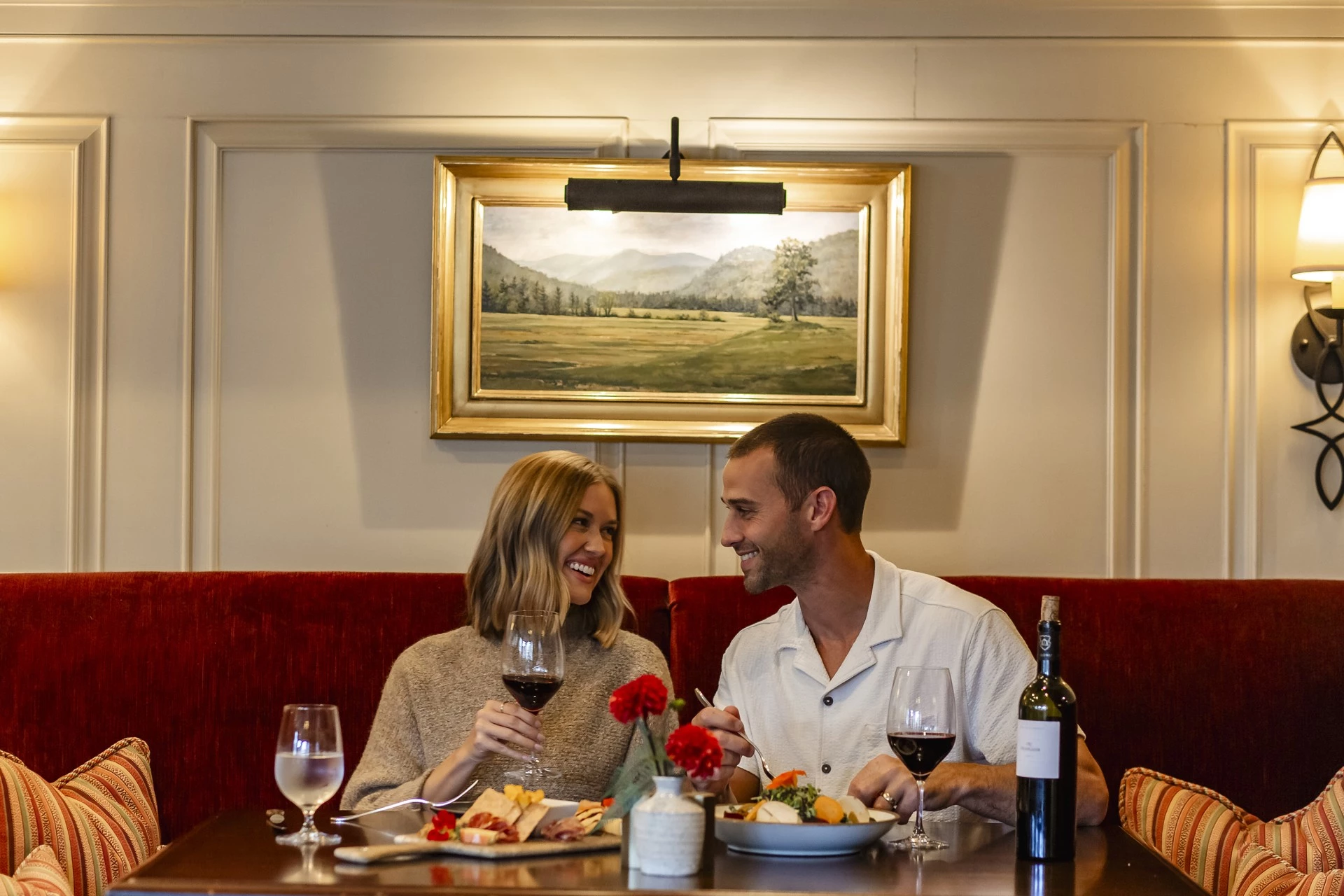 a man and woman sitting at a table with food and wine