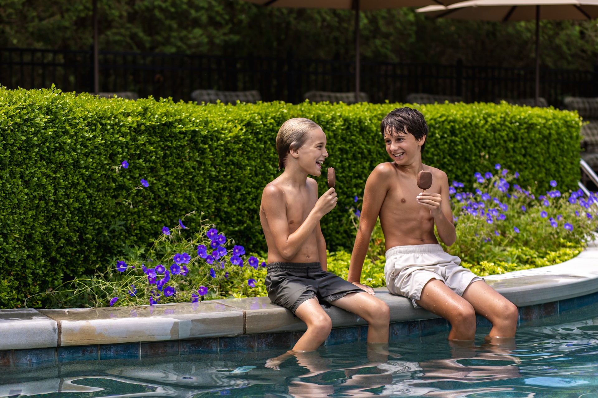 two boys sitting on a pool edge eating ice cream