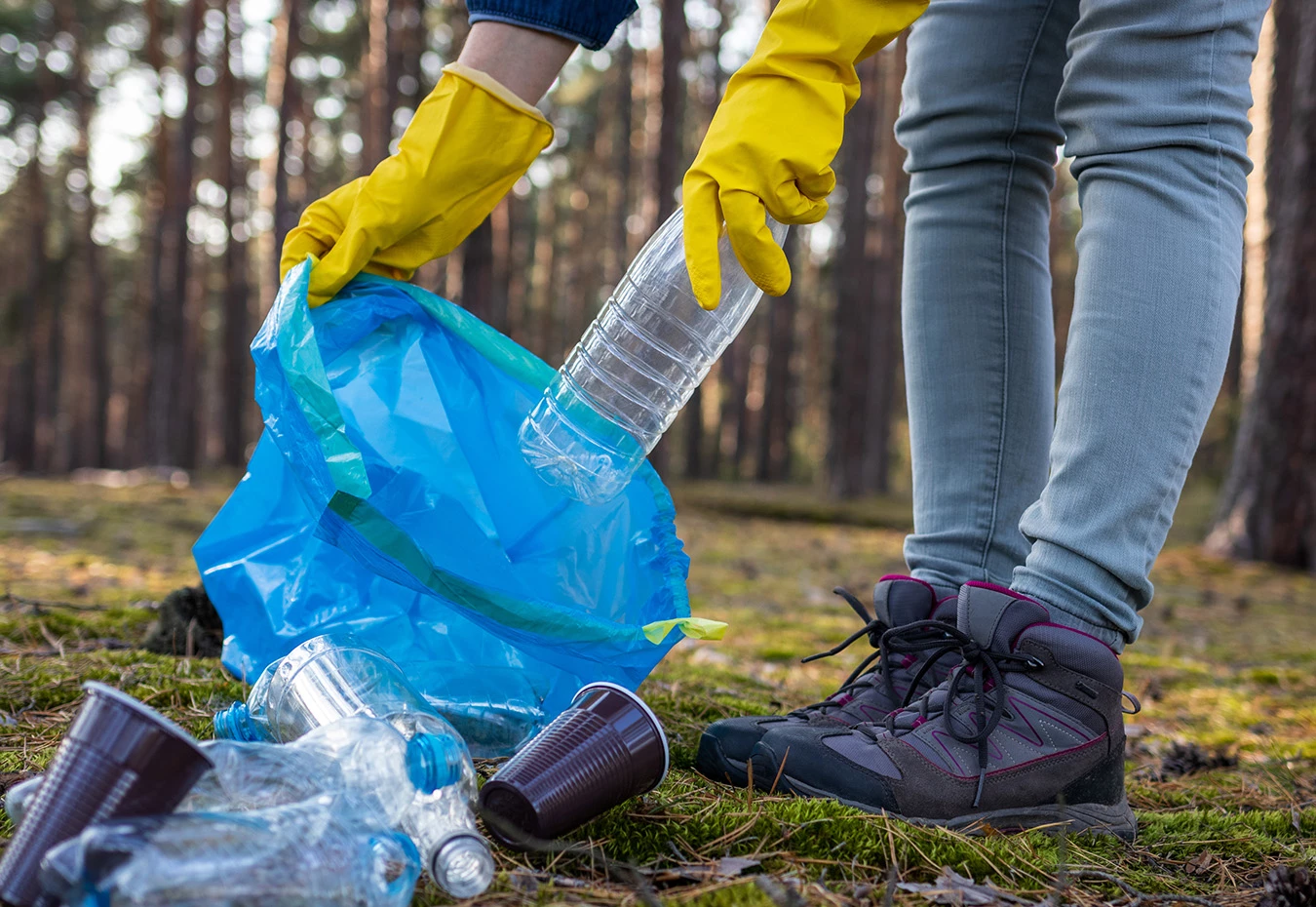 a person wearing gloves putting a plastic bottle into a blue bag