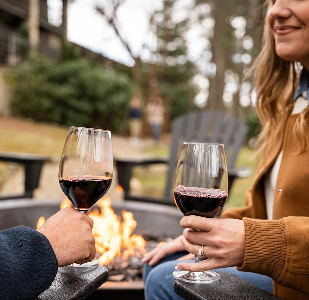 a couple of people holding wine glasses in front of a fire pit