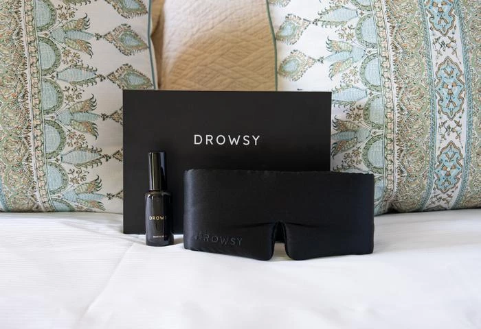 a black eye mask and a bottle of nail polish on a bed