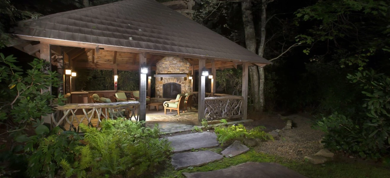a gazebo with a fireplace and chairs in the middle of the woods