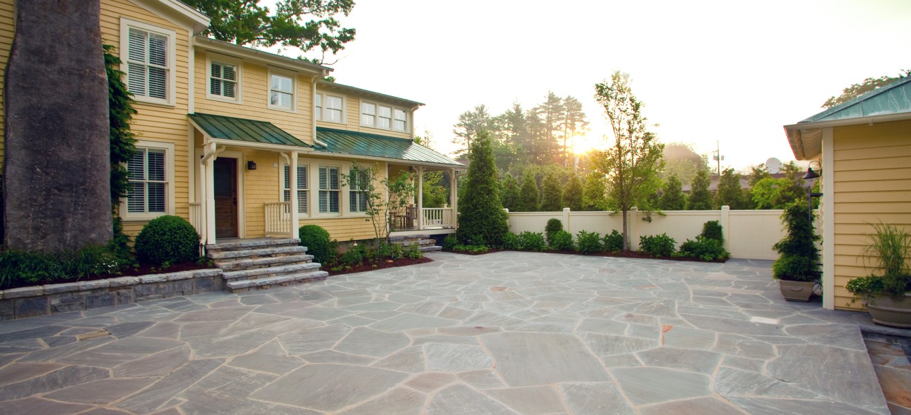 a large stone patio with a house and trees in the background