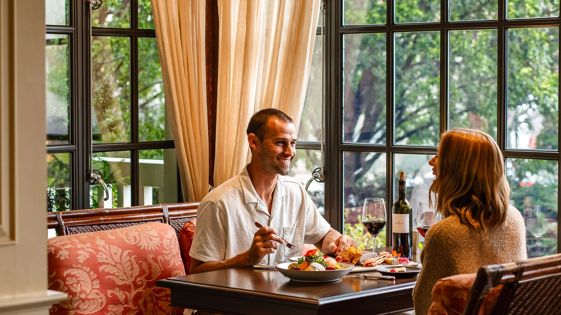 a man and woman sitting at a table with food and wine