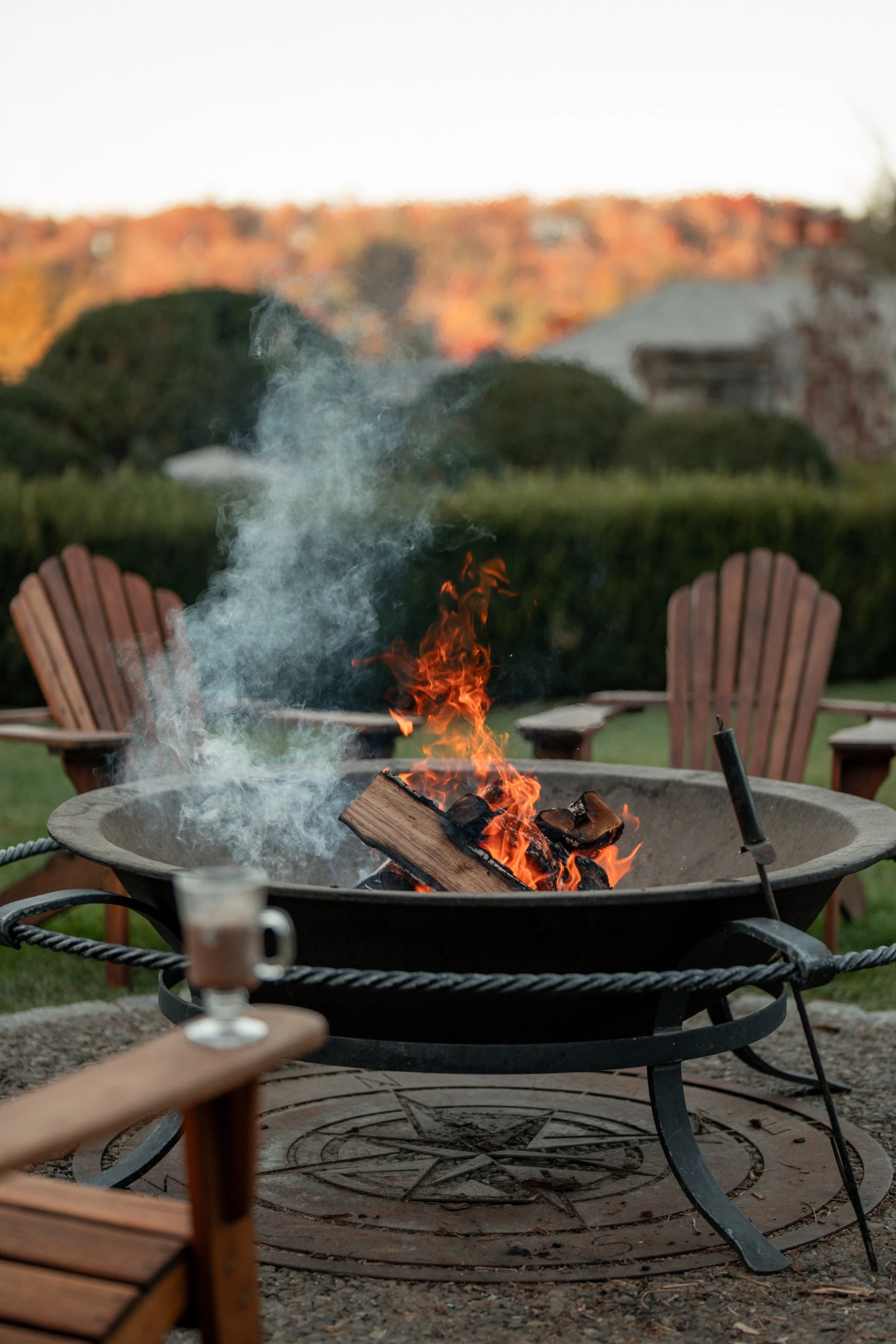 a fire pit with wood burning and chairs in the background