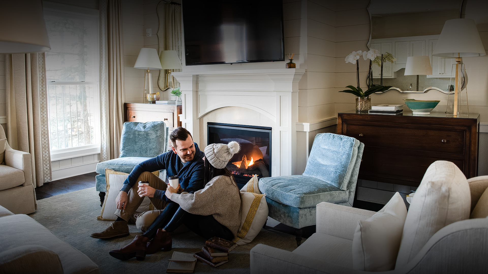 a man and woman sitting on the floor in front of a fireplace