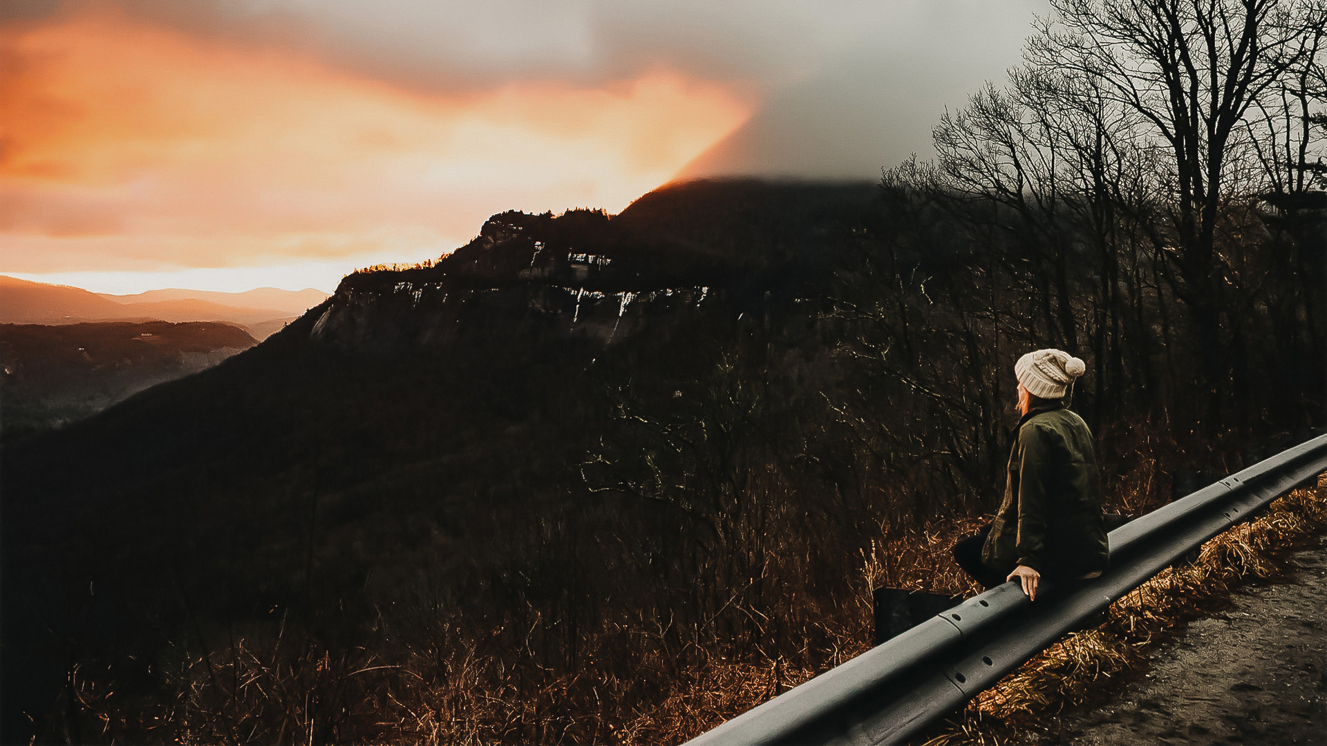 a person sitting on a railing overlooking a mountain