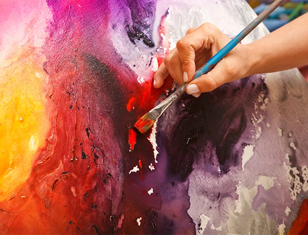 a hand holding a paintbrush painting a colorful painting